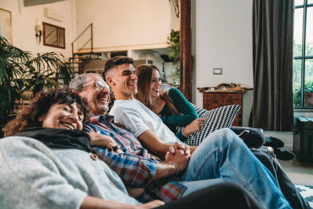 Family with two adolescent children are watching TV on the sofa at home Family with two adolescent children are watching TV on the sofa at home. They are spending time together. streaming service stock pictures, royalty-free photos & images