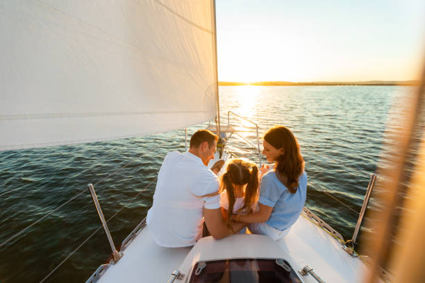 Family Yacht Sailing, Parents And Daughter Sitting On Deck, Back-View Family Yacht Sailing. Parents And Little Daughter Sitting Together On Sailboat Deck Hugging Enjoying Sea Trip. Back View, Free Space affluent lifestyles stock pictures, royalty-free photos & images