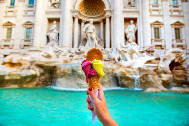 Hand holding colorful gelato in front of famous iconic Trevi Fountain at Rome, Italy.