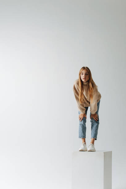 Far shot of a teenage girl standing on a white cube, leaning forward stock photo
