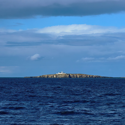 The rugged, scenic Farne Islands from Seahouses in sharp sunlight, with a chance cloud formation seeming to mirror the island’s form on the horizon.