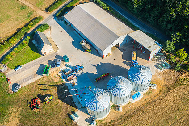 Farm outbuildings barns silos tractors agricultural machinery aerial view Aerial photo of modern farm, tractors, harvesters and agricultural equipment, barns and grain silos. ProPhoto RGB profile for maximum color fidelity and gamut. agricultural building stock pictures, royalty-free photos & images
