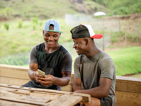 Two male farm workers sitting at a cafe table looking at a mobile phone and smiling
