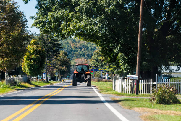 Farmer tractor driving on paved rural countryside highway road in Green Bank city small science town village in West Virginia stock photo