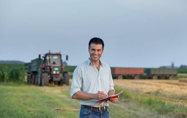 Farmer with notebook in front of tractor in field Young handsome farmer with notebook standing in field in front of tractor with trailer crop yield stock pictures, royalty-free photos & images