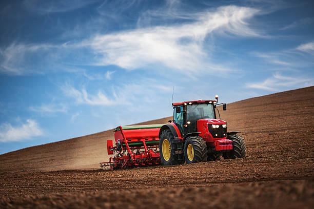 Farmer with tractor seeding crops at field Farmer in tractor preparing farmland with seedbed for the next year sports field stock pictures, royalty-free photos & images