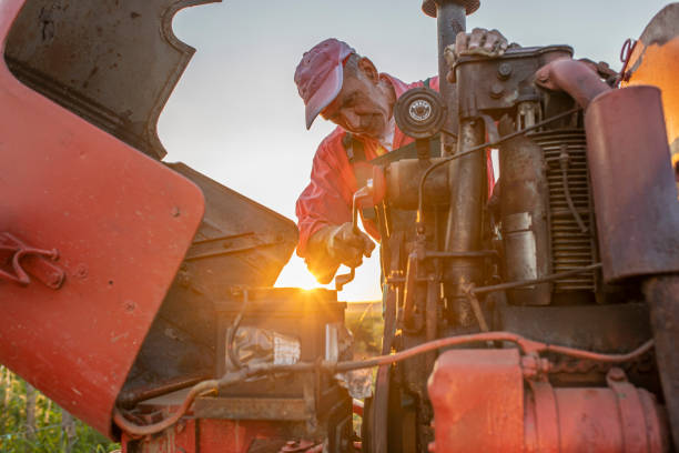 Farmer working on agricultural equipment on a farm Older farmer repairing agricultural equipment on a farm during sunset agricultural machinery stock pictures, royalty-free photos & images