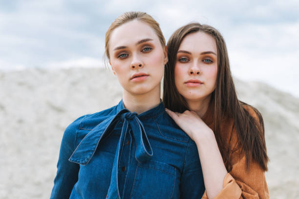 Fashion beauty portrait of young women sisters in brown organic velvet jeans shirts on the desert background stock photo