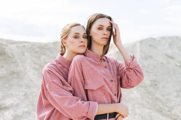 Fashion beauty portrait of young women sisters in pink organic velvet shirts on desert background stock photo