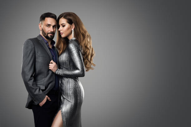 Fashion Couple Man Model Woman. Luxury Glamour Girl in Silver Dress and Elegant man in Suit. Evening Hairstyle and Make up over Gray Background stock photo