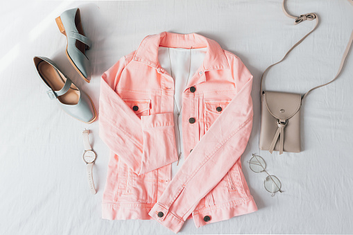 Beautiful trendy pale pink jacket and accessories on white bed sheet background. Fashion concept. Flat lay, top view.