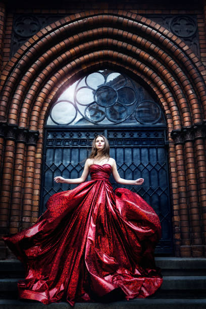 Fashion Model near Medieval Castle Gate Door, Woman Beauty Glamour Portrait in Elegant Waving Red Dress Fashion Model near Medieval Castle Gate Door, Woman Beauty Glamour Portrait in Elegant Waving Red sparkling Dress evening gown stock pictures, royalty-free photos & images