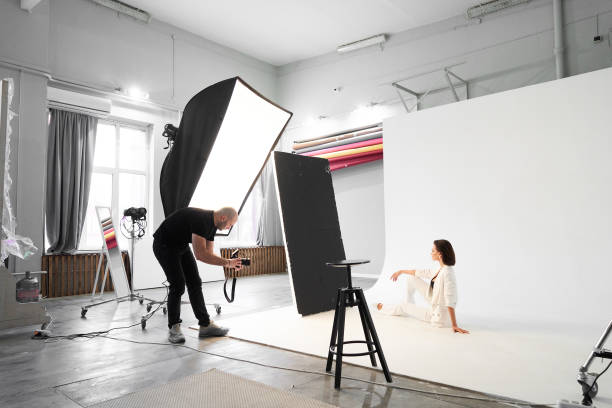 Fashion photography in a photo studio. Professional male photographer taking pictures of beautiful woman model on camera, backstage stock photo