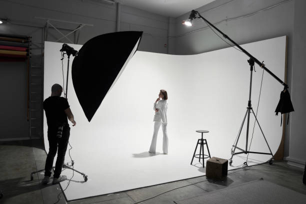 Fashion photography in a photo studio. Professional male photographer taking pictures of beautiful woman model on camera, backstage stock photo
