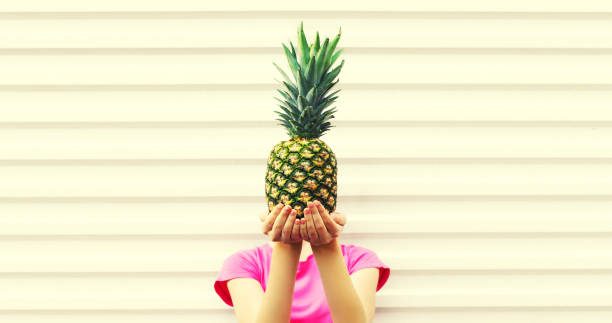 Fashion portrait woman covering her head and holding pineapple on white background, blank copy space for advertising text stock photo