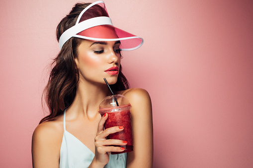Fashion pretty cool girl drinks from cup over pink background
