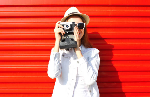 mode vrij jonge vrouw nemen foto op retro camera over kleurrijke rode achtergrond - photographer stockfoto's en -beelden