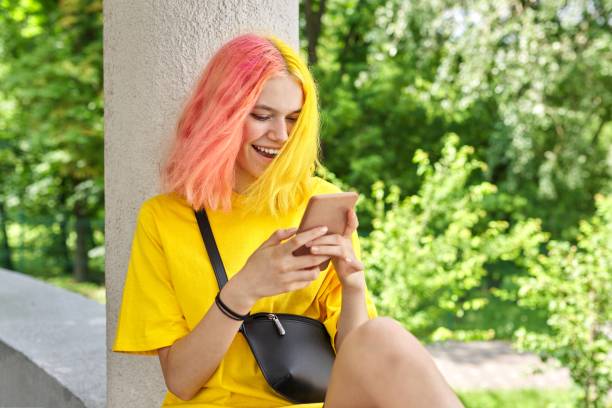 Fashionable teenager girl with colored dyed hair with a smartphone outdoors. Fashionable teenager girl with colored dyed hair with a smartphone outdoors. Smiling bright young woman in yellow t-shirt with yellow pink hair pink hair stock pictures, royalty-free photos & images