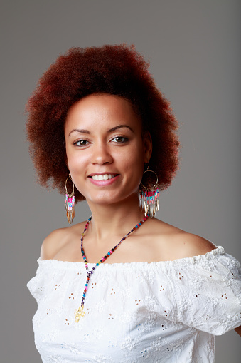 Fashionable young Black woman wearing beaded jewellery smiling happily at the camera in a studio portrait