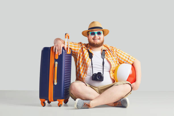 Fat funny man with a beard in a summer shirt in a hat with a suitcase...