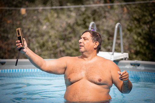 fat-man-in-the-swimming-pool-happy-mature-man-using-phone-in-a-pool-picture-id1174304308