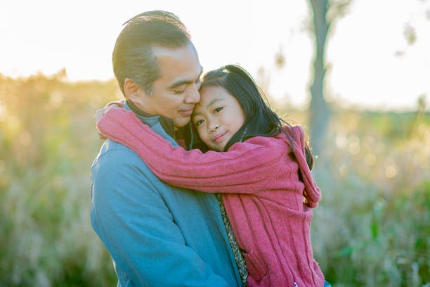 Father and daughter hold each other outside and reflect peacefully An asian man looks sensitively at his daughter, who is hugging him and gazing into the distance. filipino family stock pictures, royalty-free photos & images