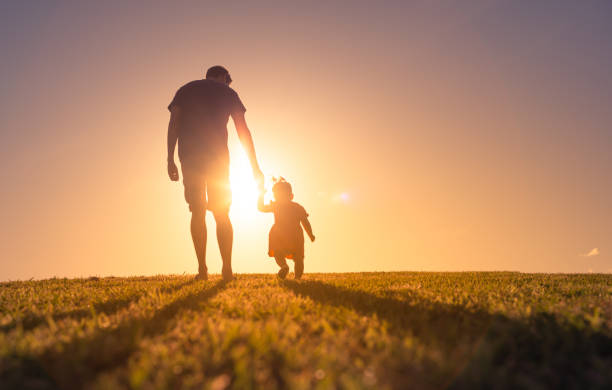 Father and daughter holding hands and walking at sunset outdoors. stock photo