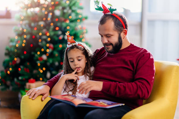 Father and his cute daughter reading Christmas fairy tales Man with beard wearing red sweater and his little daughter with dark hair reading Christmas fairy tales christmas story telling stock pictures, royalty-free photos & images