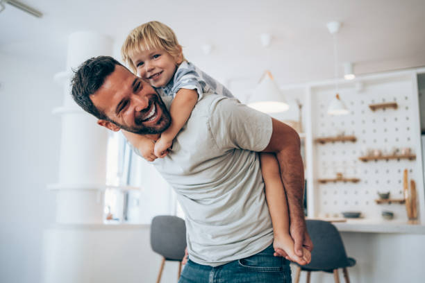 Father and little son at home. Shot of a father and his little boy spending time together at home. Happy single father and son having fun in the living room. Portrait of a father giving his son a piggyback at home. fathers day stock pictures, royalty-free photos & images