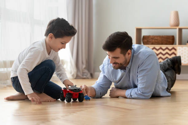pappa och lille son leker leksaksbilar på varmt golv - house with 2 cars bildbanksfoton och bilder