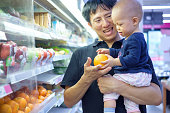 父と息子は、スーパーで買い物。お父さんとかわいい小さなアジア 12 ヶ月/1 年古い赤ちゃん男の子の子供の食料品店で果物を選択する笑みを浮かべて、子供は最初概念を体験します。