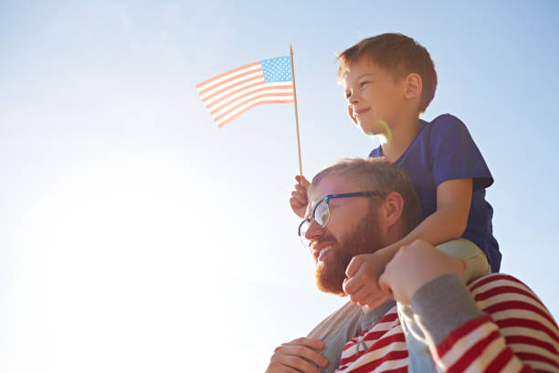Father and son at parade Patriotic family with American flag visiting parade devoted to Independence Day happy fourth of july stock pictures, royalty-free photos & images