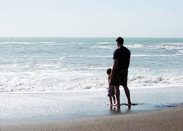 Father and Son at the Beach High Key image of father and son at the ocean's edge; Concept for Environmental Legacy? divorce beach stock pictures, royalty-free photos & images