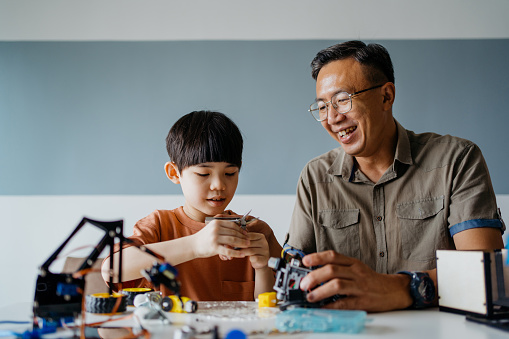 Image of an Asian Chinese young boy building a robot toy together with his father in living room