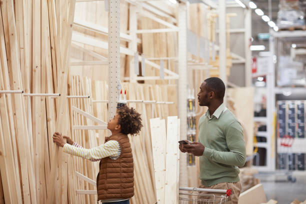 Father and Son Buying Wooden Panels in Construction Store Side view portrait of African-American father and son shopping together in hardware store, focus on boy choosing wooden boards for construction, copy space lumber stock pictures, royalty-free photos & images