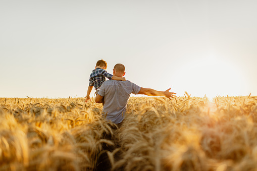 Father and son having fun on agricultural field against sky