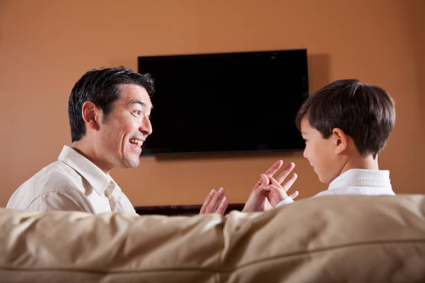Father and son on couch with TV in background Little boy (6 years) and father (40s) talking on couch, TV in background.  Both mixed race, Asian/Caucasian.  Main focus on father. asian kids watching tv stock pictures, royalty-free photos & images