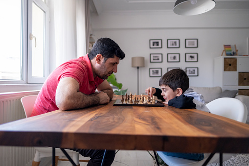 Father and son playing chess at home together. Family at home.