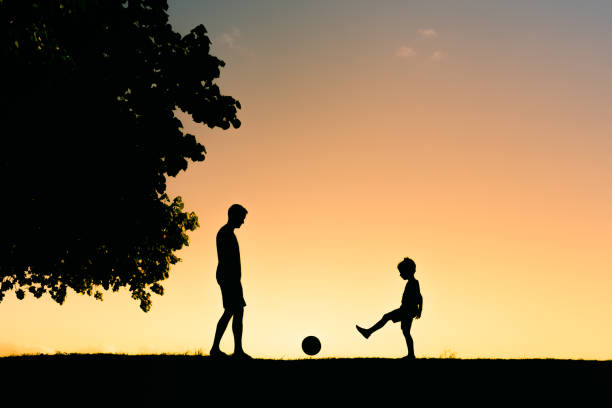 Father and son playing soccer outdoors at sunset. stock photo