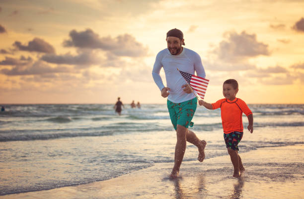 Father and son running with an american flag on the beach stock photo