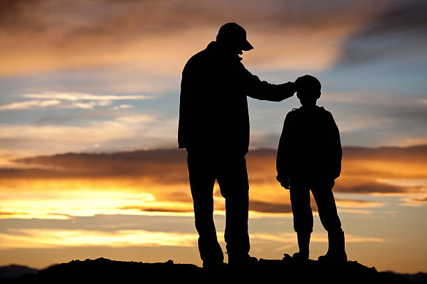 Father and Son Silhouette A silhouette of a father and son sharing a tender moment. Additional themes include single parent, parenting, father, fatherhood, stepfather, consoling, care, unity, family, bonding, encouragement, coach, role model, instructor, guidance, and comforting.  fathers day stock pictures, royalty-free photos & images
