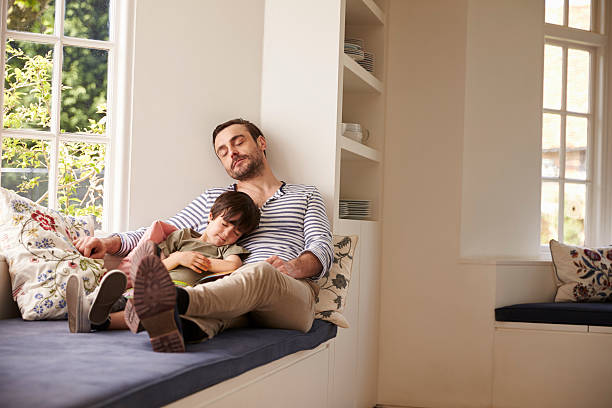 Father And Son Sleeping On Window Seat At Home Together Father And Son Sleeping On Window Seat At Home Together alcove window seat stock pictures, royalty-free photos & images