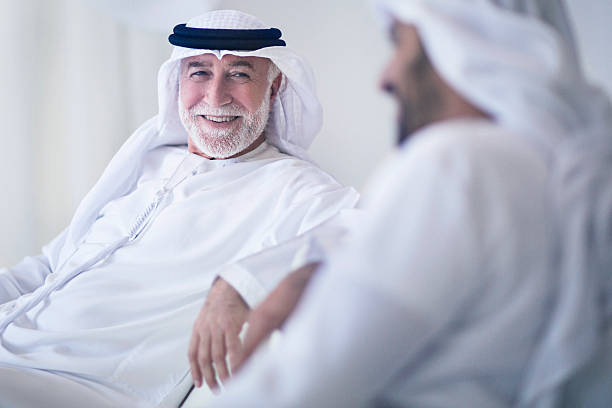 Father and son talking Middle Eastern father and son having a good time talking at home, both wearing the traditional Dishdasha. old arab man stock pictures, royalty-free photos & images