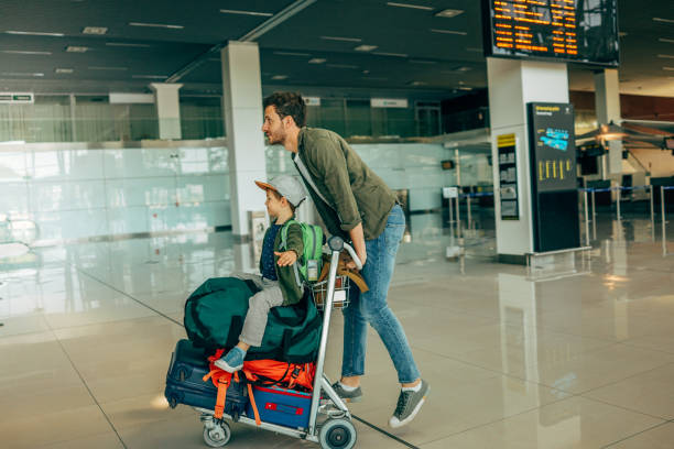 Father and son traveling together Photo of a cheerful little boy and his father, who travel together, pushing a luggage cart at the airport luggage cart stock pictures, royalty-free photos & images
