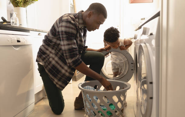 Father and son washing clothes in washing machine African American father and son washing clothes in washing machine at home grooming product stock pictures, royalty-free photos & images