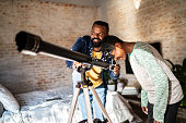 istock Father and son with telescope looking at sky from home 1332136920