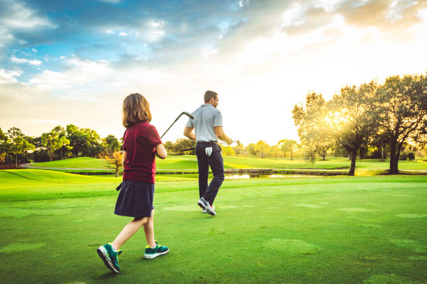 Father and young daughter on the golf course together playing a round of golf with family stock photo
