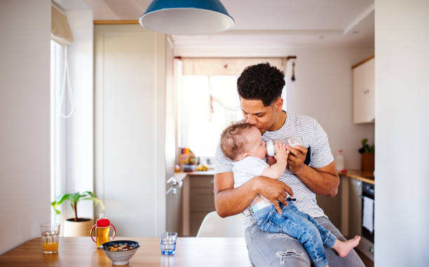 un padre alimenta a un niño pequeño en casa. - baby formula fotografías e imágenes de stock