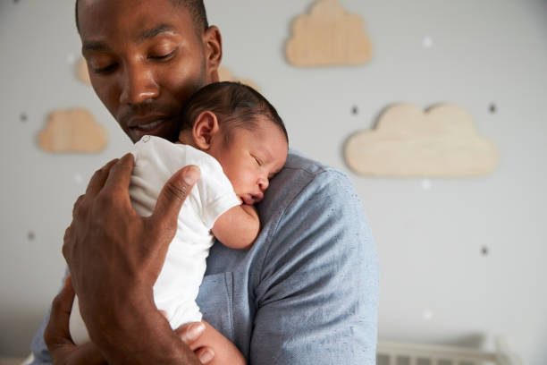 vader bedrijf pasgeboren zoontje in kinderkamer - newborn stockfoto's en -beelden
