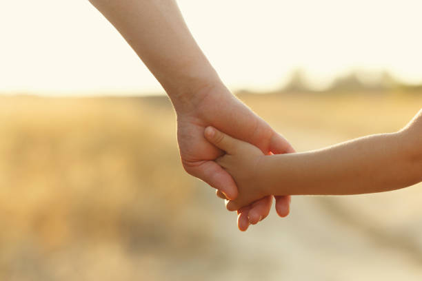 Father holds daughter by the hand Father holds daughter by the hand. Shooting close-up. In the background, out of focus is a country road. Support on the way. holding hands stock pictures, royalty-free photos & images